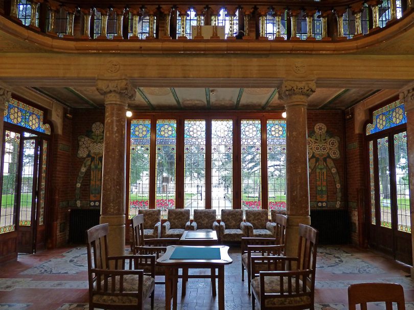 ein großer Saal mit großen Glasfenstern an allen Wänden, eine hohe gewölbte Decke und in der Mitte ein Holztisch mit vier Holztischen drum herum