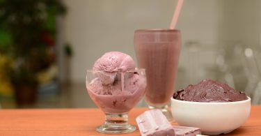 auf einem Tisch liegen zwei schokoeis am Stil, ein glas mit schokoeis ein hoher Becher und ein tiefer Teller ebenfalls mit schokoeis