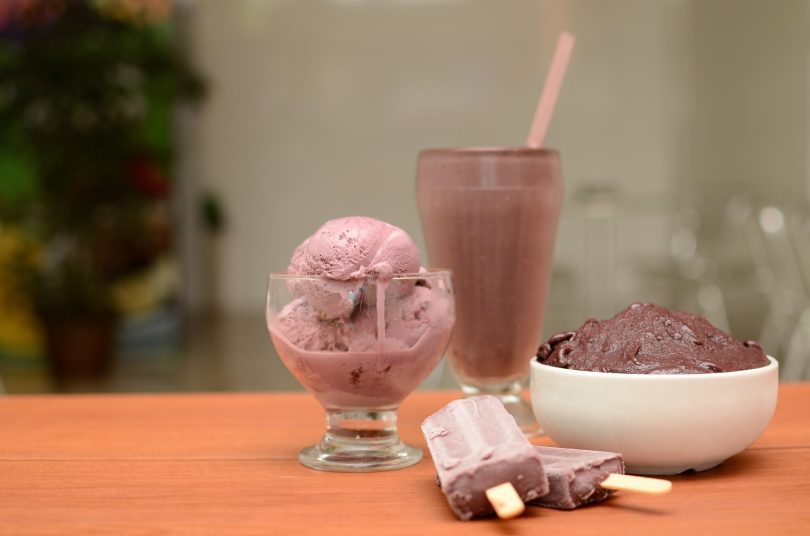 auf einem Tisch liegen zwei schokoeis am Stil, ein glas mit schokoeis ein hoher Becher und ein tiefer Teller ebenfalls mit schokoeis