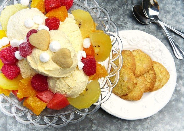 ein Obstbecher mit Vanilleeis von oben gesehen und daneben ein kleiner weißer Teller mit Keksen dazu
