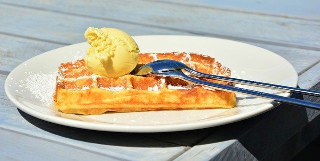 auf einem Holztisch steht ein weißer runder Teller mit einer Waffel und eine Kugel Vanilleeis darauf