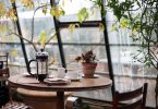 Kleiner Wintergarten mit Pflanzen, einem kleinen runden Holztisch auf dem eine kleine Topfpflanze , eine Tasse und eine Teekanne stehen