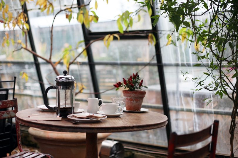 Kleiner Wintergarten mit Pflanzen, einem kleinen runden Holztisch auf dem eine kleine Topfpflanze , eine Tasse und eine Teekanne stehen