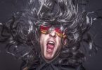 ein Mann mit dunkelgrauen Haaren, einer rot gelben Faschingsbrille und einem grauem Hemd der mit offenem Mund schreit
