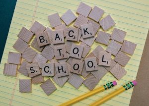 Scrabble Spielsteine auf gelb liniertem Papier zum Satz back to school aufgereiht und zwei gelbe Bleistifte daneben