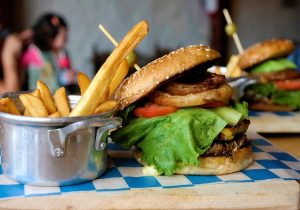 üppiger Hamburger mit Pommes Frites in Metaltöpfchen auf Holzbrett mit blau weiss karierter Serviette