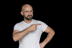 Glatzköpfiger Man mit weisem t-Shirt der mit dem Finger nach rechts zeigt