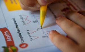 zwei Kinderhände mit einem gelben Bleistift bei der Lösung verschiedener Summen