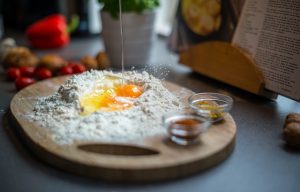 Brett mit Weissmehl, zwei Eiern in der Mitte und zwei kleinen Glasschälchen an der Seite mit Gewürzen