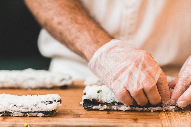 eine Person mit weißen Gummihandschuhen die gerade sushi Rollen macht