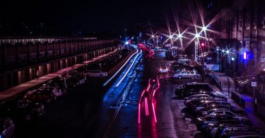 Strasse einer Großstadt bei Nacht mit roten blauen Lichtern der Autos und Parkplätze links und rechts