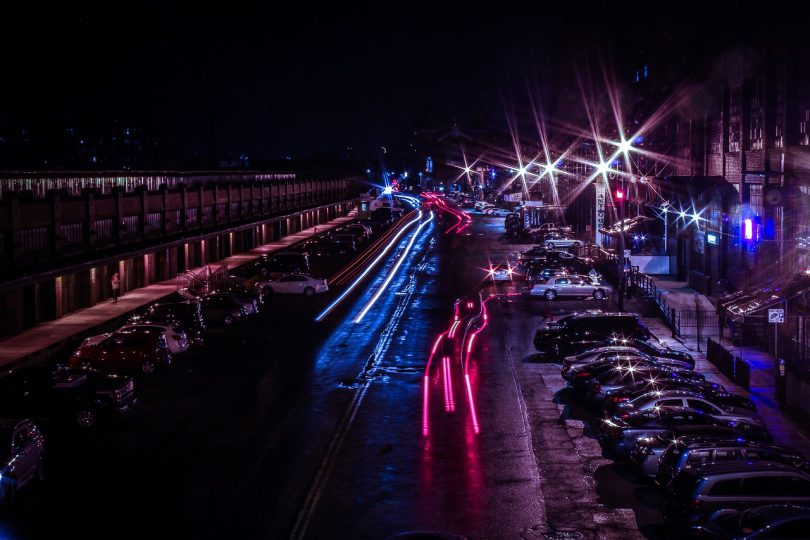 Strasse einer Großstadt bei Nacht mit roten blauen Lichtern der Autos und Parkplätze links und rechts