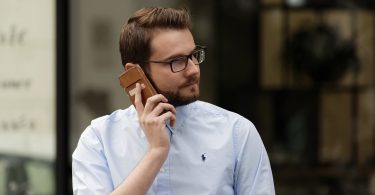 Man mit hellblauem Hemd und Brille der mit seinem Handy telefoniert