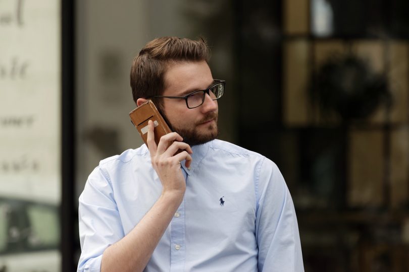 Man mit hellblauem Hemd und Brille der mit seinem Handy telefoniert