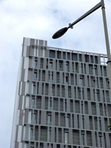 Modernes Hochhaus in grau, bewölkter Himmel, und Teil einer Strassenlaterne