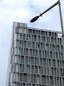 Modernes Hochhaus in grau, bewölkter Himmel, und Teil einer Strassenlaterne