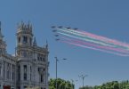 sieben Militärflugzeuge die in Dreiecks Formation die spanische Flagge mit Rauch über einem Rathaus überfliegen