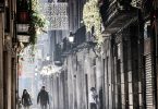 Fussgängerzone in Barcelona, ein Pärchen läuft unter der warmen Wintersonne die Gasse entlang, ein Teil der Weihnachtsbeleutung ist schon aufgehängt
