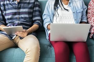ein Student und eine Studentin die auf einem grünem Sofa sitzen, sie mit einem Laptop und er mit einer Tablet