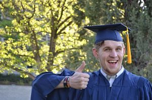 ein junger Mann der den Daumen nach oben zeigt und lächelt weil der seinen Bachelor bestanden hat, ausserdem trägt er die traditionelle Toga und Hut in blau