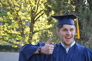 ein junger Mann der den Daumen nach oben zeigt und lächelt weil der seinen Bachelor bestanden hat, ausserdem trägt er die traditionelle Toga und Hut in blau