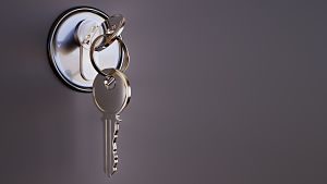 graue Tür mit verchromten Schlüsselzilinder und einem Schlüssel drin und ein zweiter hängt dran