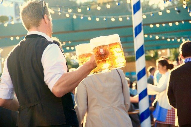 ein Kellner in weißem Hemd und schwarzer Weste der vier Bierkrüge in der Halt hält und durch die Menschenmengen läuft