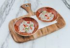 ein Holzbrett auf weissem Marmor, darauf eine weisse Serviette und zwei braune kleine Schüsseln mit ceviche