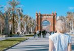 Die Allee zum Triumph Tor in Barcelona, es ist eine junge blonde Frau mit weisem T-shirt von hinten zu sehen, die auf einem Arm eine geometrische Figur und auf dem anderen Blumenzweige tätowiert hat