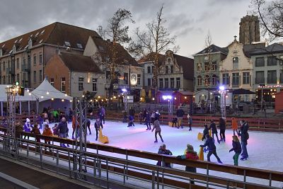 eine Schlittschuhbahn auf einem Marktplatz mit vielen Leuten darauf, Kinder mit Fahrhilfen und weihnachtslichter über der Bahn und in den bäumen