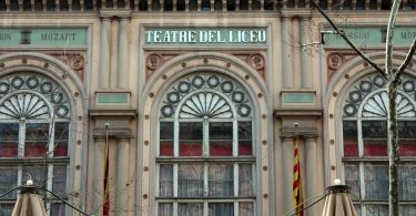 Der Eingang der Teatre del Liceu in Barcelona, beige Fassade mit hellgrünen Details und einer spanischen Flagge links und einer katalanischen Flagge rechts von der Tür