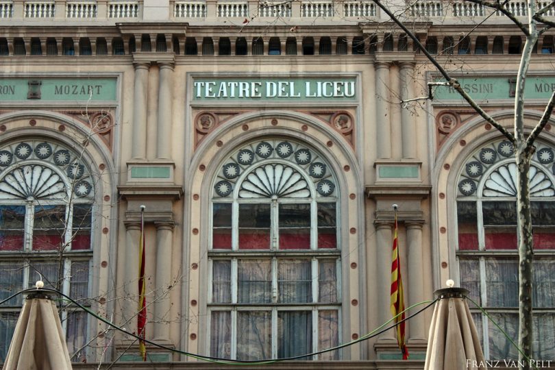 Der Eingang der Teatre del Liceu in Barcelona, beige Fassade mit hellgrünen Details und einer spanischen Flagge links und einer katalanischen Flagge rechts von der Tür