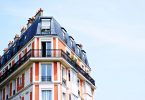 ein Apartment Hochhaus in rot und weiss gestrichen mit einem dunkelgrauem Dach, das vorletzte Stockwerk hat einen Balkon um das ganze Gebäude
