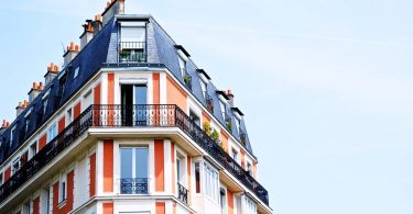ein Apartment Hochhaus in rot und weiss gestrichen mit einem dunkelgrauem Dach, das vorletzte Stockwerk hat einen Balkon um das ganze Gebäude