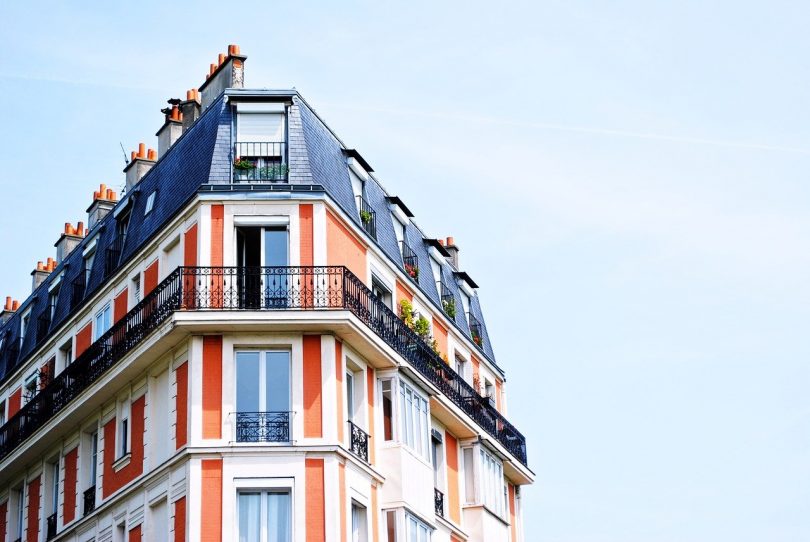 ein Apartment Hochhaus in rot und weiss gestrichen mit einem dunkelgrauem Dach, das vorletzte Stockwerk hat einen Balkon um das ganze Gebäude