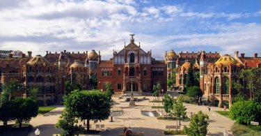 Vorderansicht der modernistischen Anlage des Krankenhauses San Pau in Barcelona, Gebäude in roten färben und ein kleiner Park davor