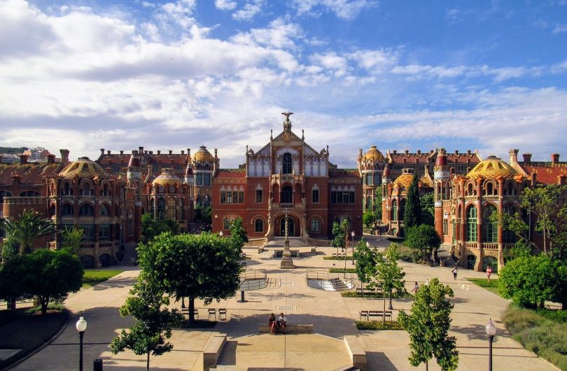 Vorderansicht der modernistischen Anlage des Krankenhauses San Pau in Barcelona, Gebäude in roten färben und ein kleiner Park davor