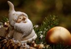ein weissgekleideter Nikolaus auf einem Tannenzwei, daneben ein länglicher Tannenzapfen und vor ihm liegt eine goldenen Kugel