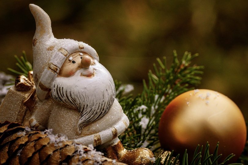 ein weissgekleideter Nikolaus auf einem Tannenzwei, daneben ein länglicher Tannenzapfen und vor ihm liegt eine goldenen Kugel