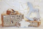 drei Geschenke in braunem Geschenkpapier mit silberner Schrift, Schneeflocken und Schneemännern, mit einem silbernem Band, einem kleinem weissen Schaukelpferd und im Hintergrund eine Lichterkette