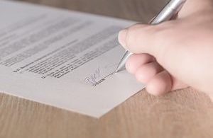 zu sehen ist ein Blatt eines deutschen Mietvertrags der gerade von jemandem mit einem silber färbenden und blauschreibenden Kugelschreiber unterzeichnet wird