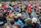 Eine breite Alles voller rennender Leute die an einem Marathon teilnehmen, der Boden ist nass aber es regnet nicht