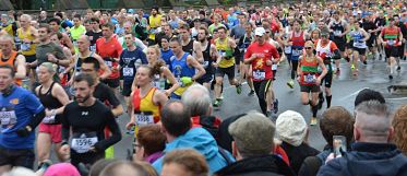 Eine breite Alles voller rennender Leute die an einem Marathon teilnehmen, der Boden ist nass aber es regnet nicht