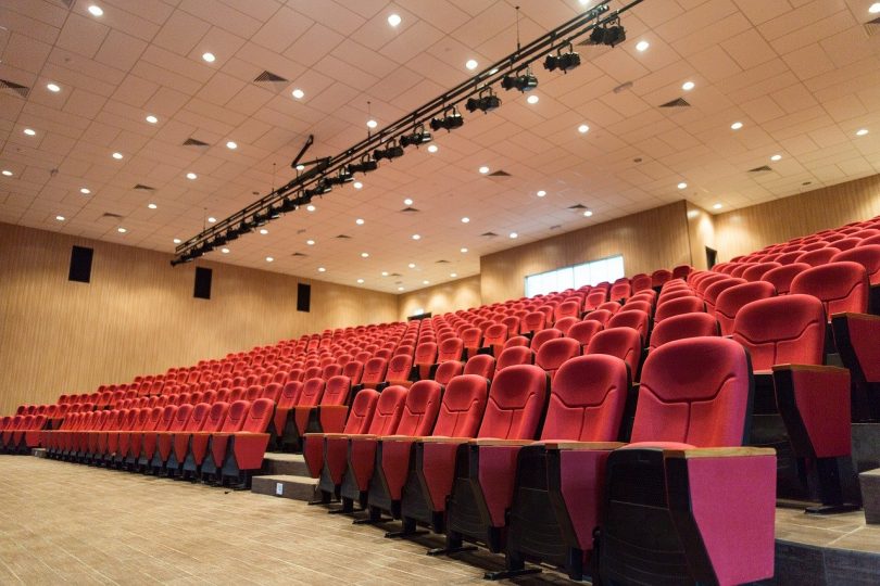 ein leerer beleuchteter Kinosaal mit roten Sesseln und Beigem Teppichboden
