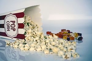 eine umgefallene Popcorntüte aus der das Popcorn rausgefallen ist und daneben eine Handvoll Gummibären in verschiedenen Farben 