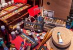 ein Schaufenster eines Bastelgeschäfts mit verschiedenen Farbtuben, Pinseln, Holzigsten mit Farben, ein Strohhut und kleine menschliche Holzfiguren