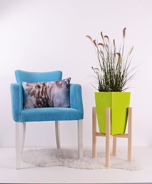 links ein moderner hellblauer Sessel mit einem hellen Kissen und rechts ein Holzgestell mit einem hellgrünen Blumentopf und hohen Gräsern darin