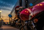ein rotes Motorrad mit einem weissen Streifen in der Mitte das bei Dämmerung in der Straße einer Stadt geparkt ist