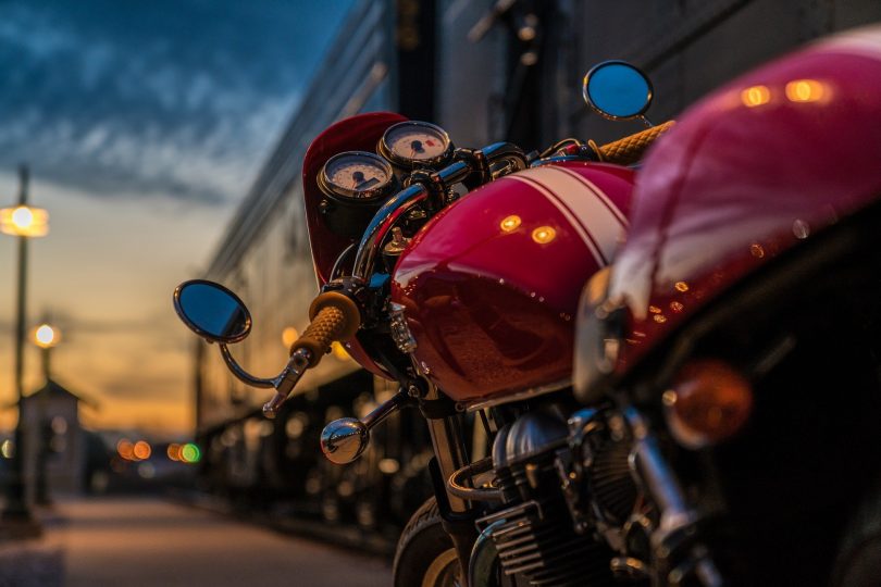 ein rotes Motorrad mit einem weissen Streifen in der Mitte das bei Dämmerung in der Straße einer Stadt geparkt ist