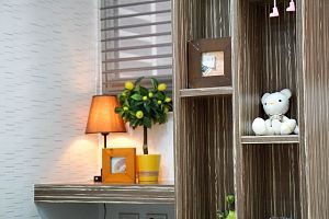 rechts ein Holzregalt mit einem Bilderrahmen und einem weissen Teddybären, links ein mittelgroßer schränk auf dem eine orangene kleine Stehlampe, ein Bilderrahmen und ein kleiner Zitronenbaum steht